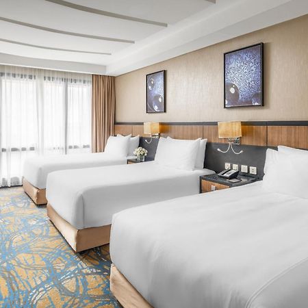 Al Ghufran Safwah Hotel Makkah La Meca Exterior foto The photo shows a hotel room featuring three neatly made beds with white linens. The room has a modern and bright design, with large windows allowing natural light to enter. There are two framed artworks on the wall above the beds, contributing to th