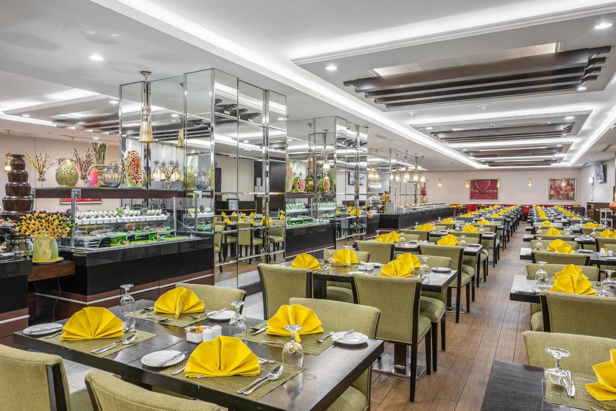 Al Ghufran Safwah Hotel Makkah La Meca Exterior foto The photo shows the interior of a restaurant. The space features neatly arranged tables, each covered with a dark tablecloth. Yellow napkins are elegantly folded at each place setting, and there are crystal glasses on the tables. In the background, t